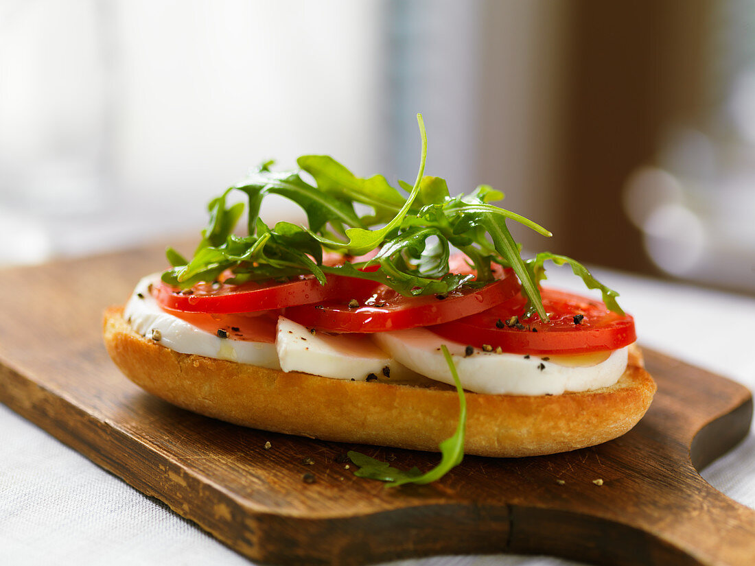 A baguette slice topped with mozzarella, tomatoes and rocket