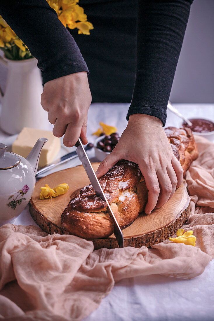 Woman slicing Braided sweet Easter bread served for breakfast with butter and jam