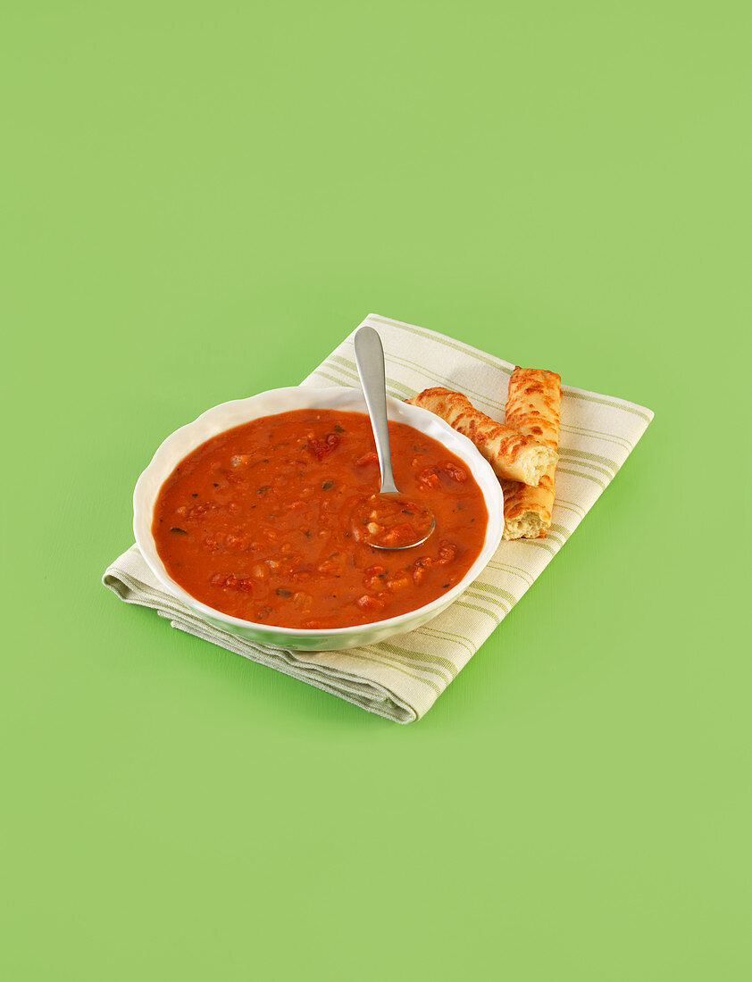 Tomaten-Fenchelsuppe serviert mit Brotstangen vor grünem Hintergrund