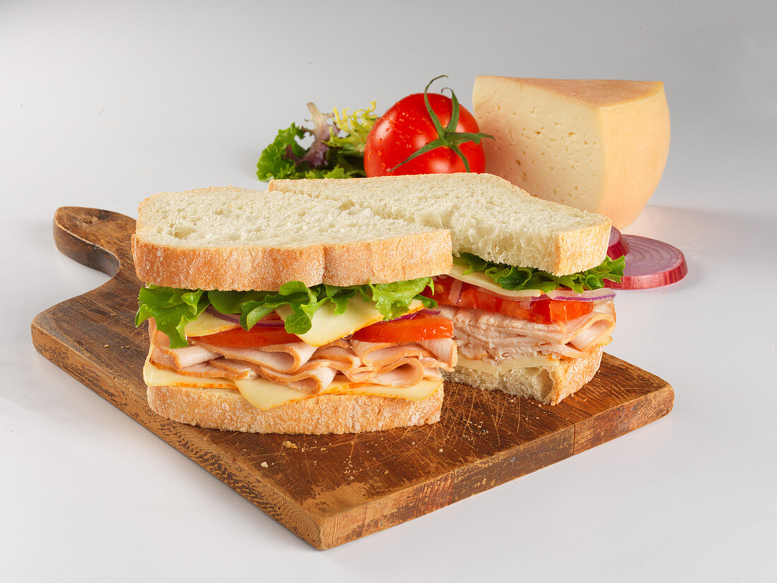 A sandwich with turkey breast, tomato, Munster cheese and salad, sliced