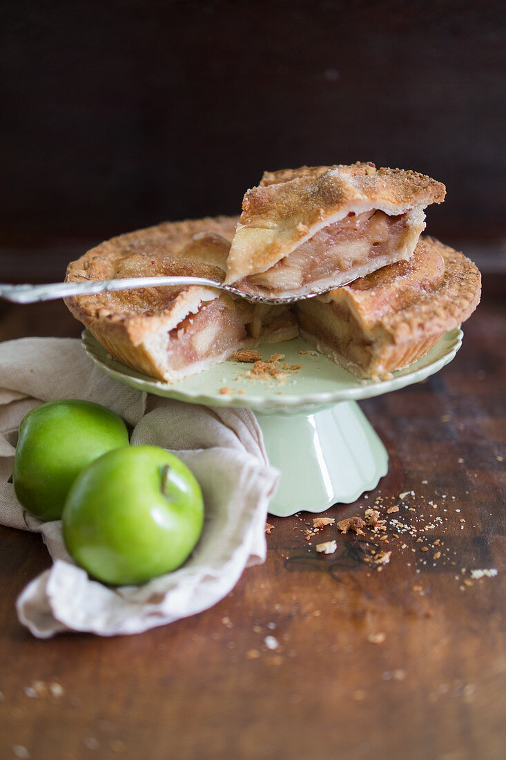 Angeschnittene Applepie auf Kuchenständer und frische grüne Äpfel