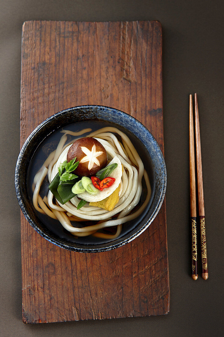 Udon-Nudelsuppe im Schälchen auf Holzbrett (Japan)