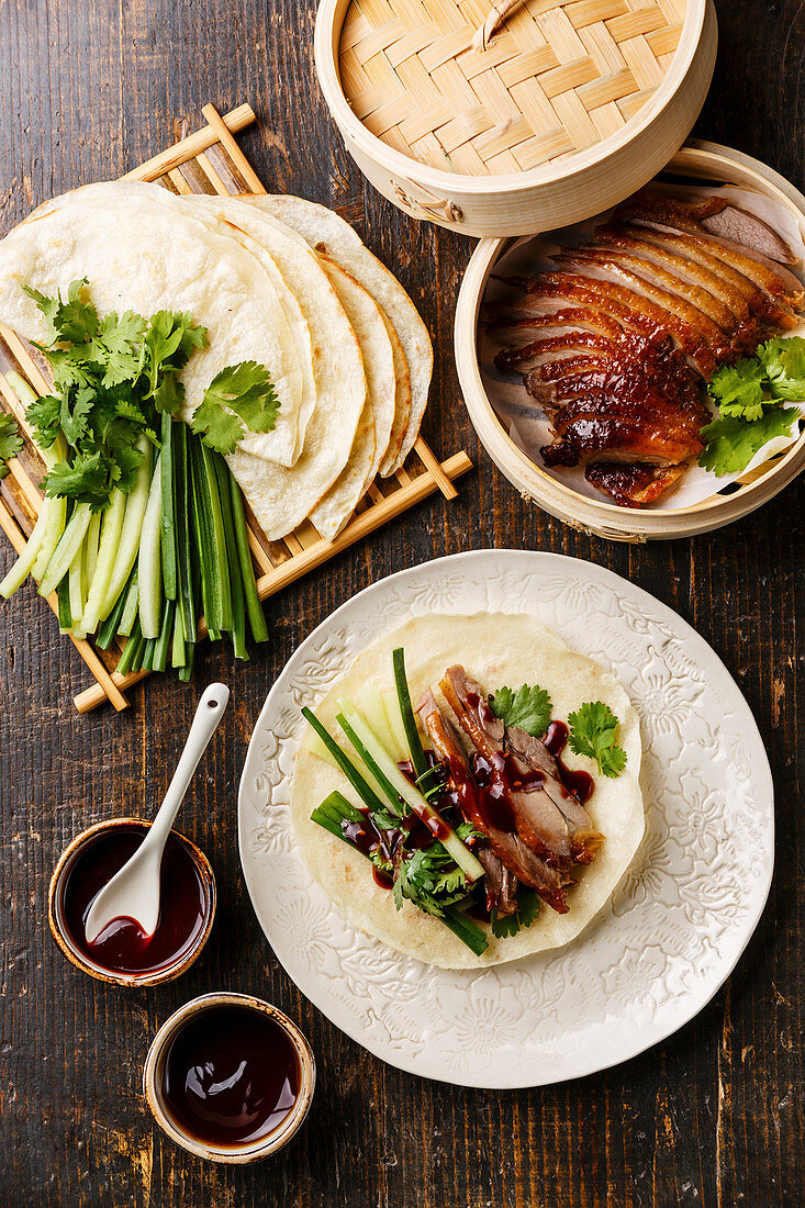 Peking Duck serving size with fresh cucumber, green onion, cilantro and roasted wheaten chinese pancakes with sauce Hoysin on wooden background