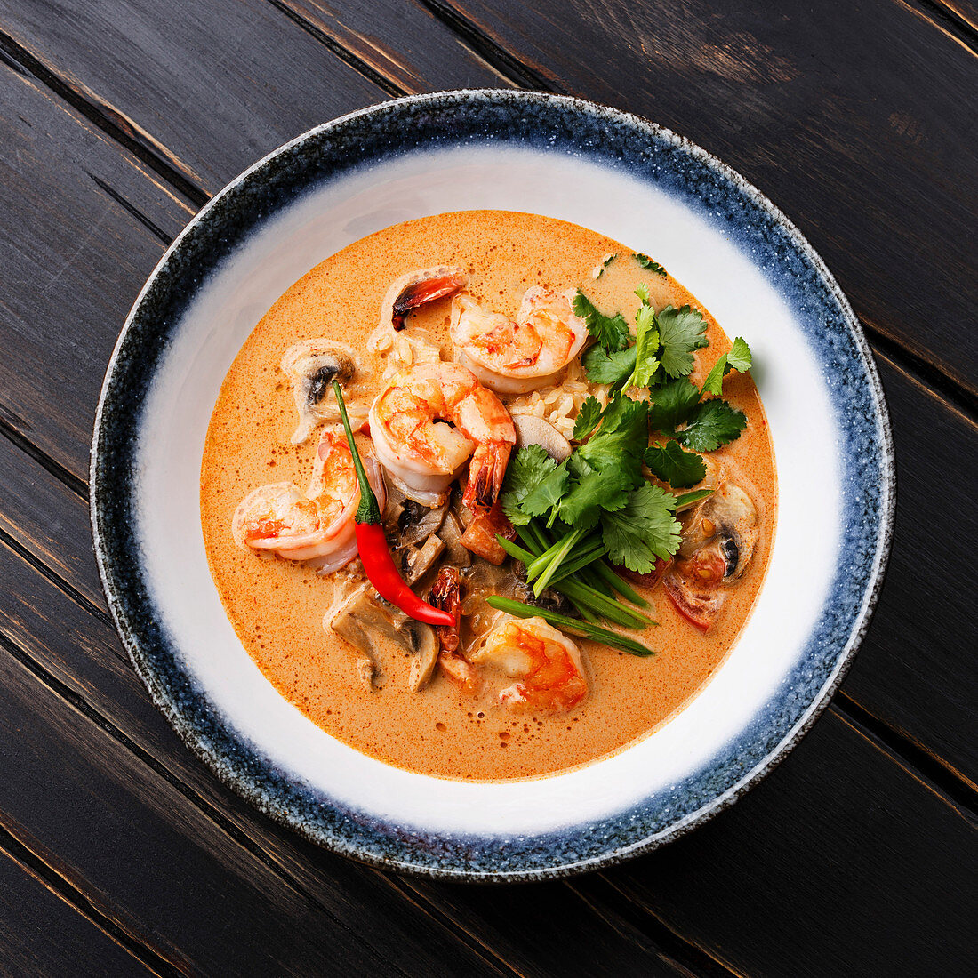 Tom Yam kung Spicy Thai soup with shrimp, seafood, coconut milk and chili pepper in bowl close-up