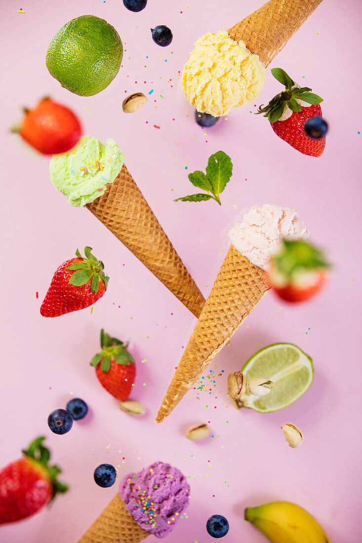 Sweet and colourful ice cream in waffle cones with sprinkles and ingredients falling or flying in motion against
