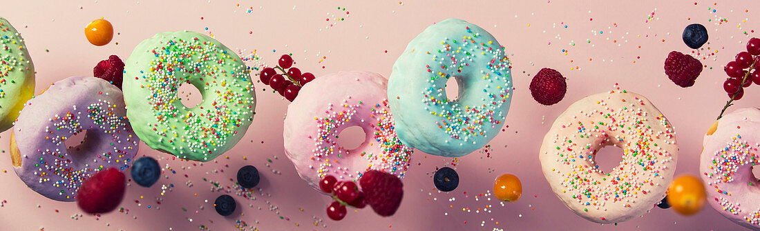 Sweet and colourful doughnuts with sprinkles and berries falling or flying in motion against pink pastel background