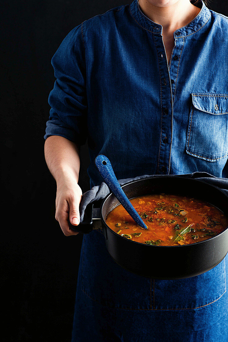 Frau hält Schmortopf mit pikanter Linsensuppe mit Gemüse