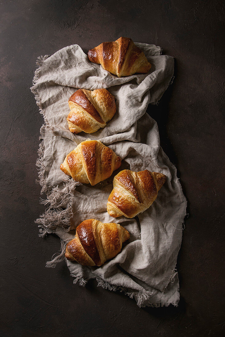 Fresh baked traditional croissant on linen cloth over dark brown texture background
