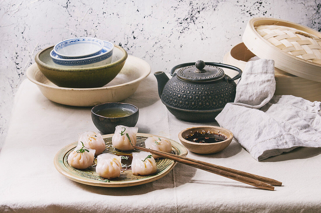 Asian steam potstickers dumplings stuffed by shrimps, served with soy sesame sauce, chopsticks, teapot, tea, bamboo steamer