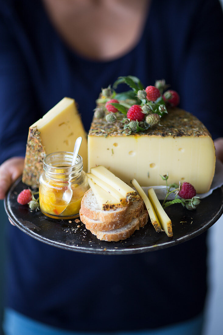 Frau hält Tablett mit Wildkräuterkäse, Brot und Chutney