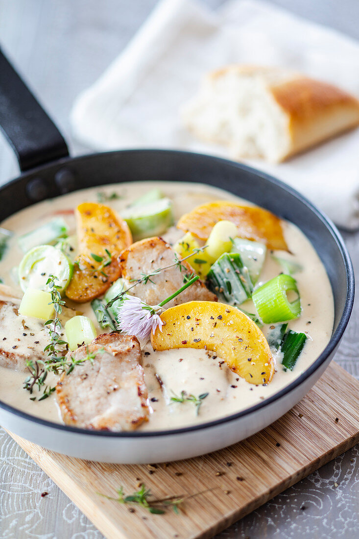 Pork fillet and roasted peaches in calvados cream sauce with chive blossoms in a pan