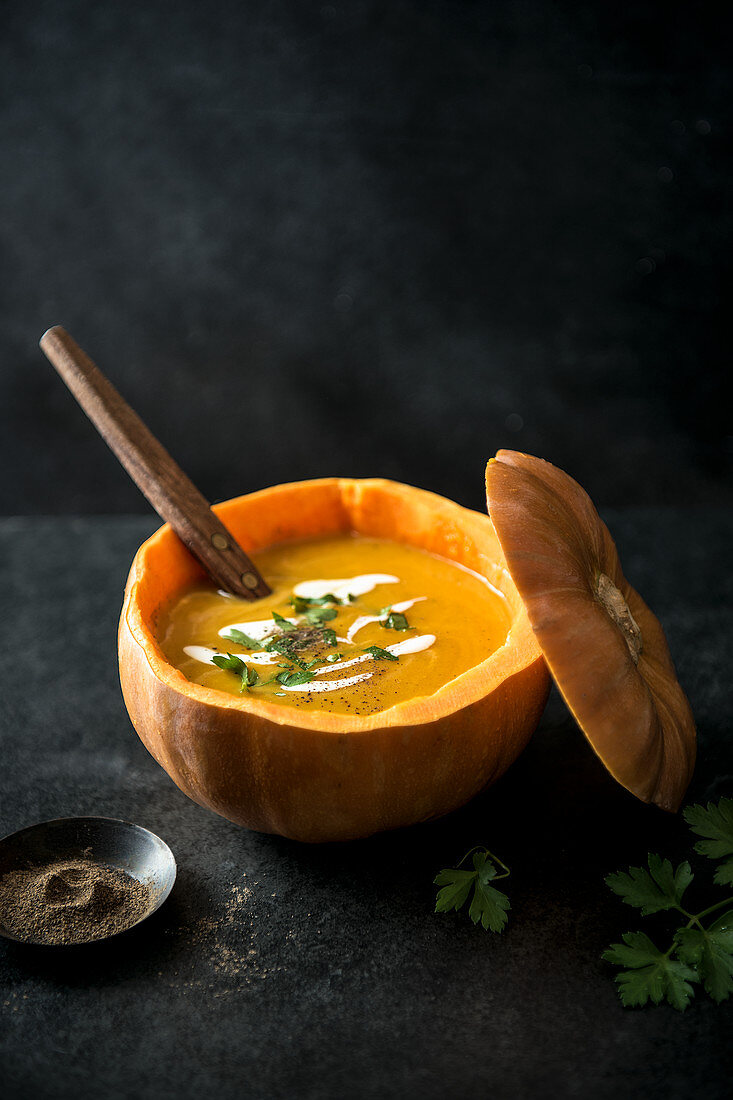 Kürbissuppe im ausgehöhlten Kürbis mit frischer Petersilie, Sahne und Pfeffer