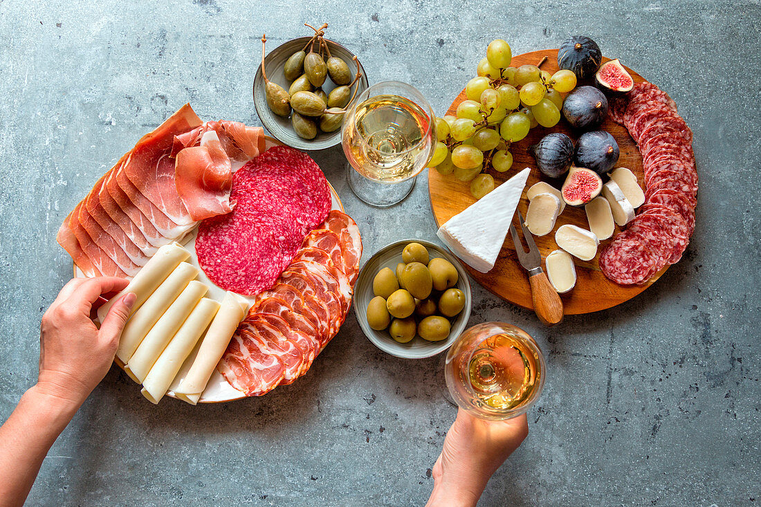 Zwei Vorspeisenplatten mit Wurst, Schinken, Käse und Obst dazu Wein, Oliven und Kapern