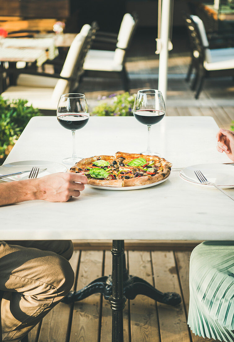 Mann und Frau mit Gemüsepizza und Rotwein an Restauranttisch im Freien