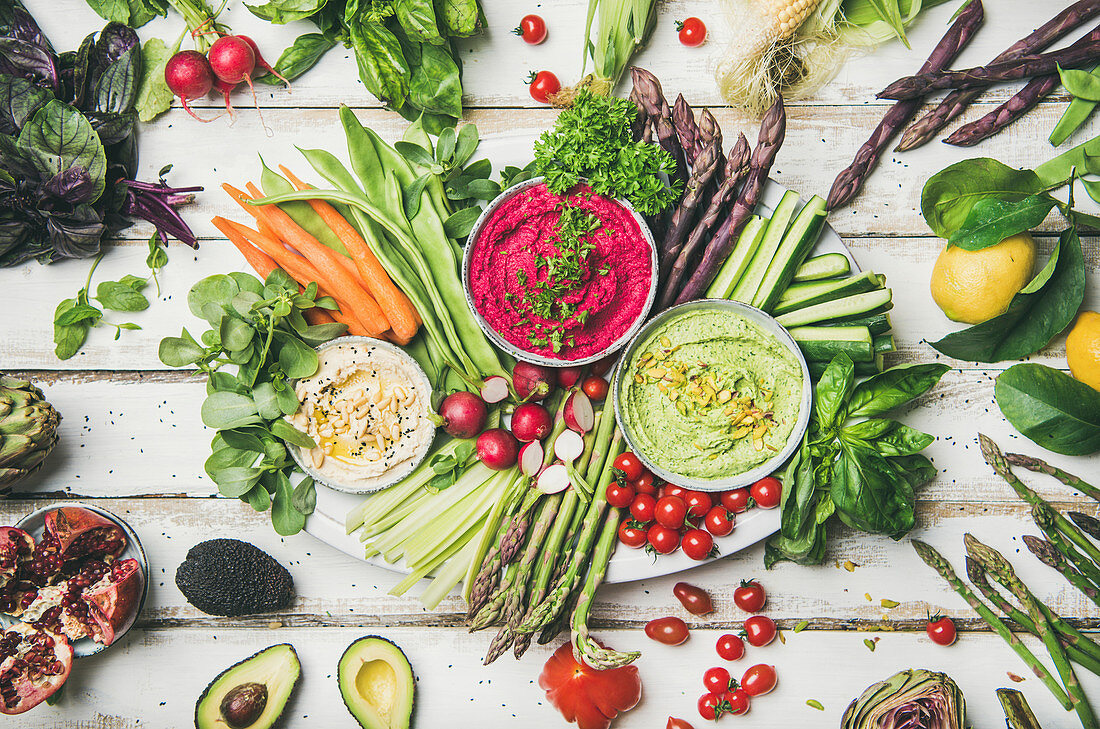 Chickpea, beetroot, spinach hummus dips with colorful vegetables and greens on white table background