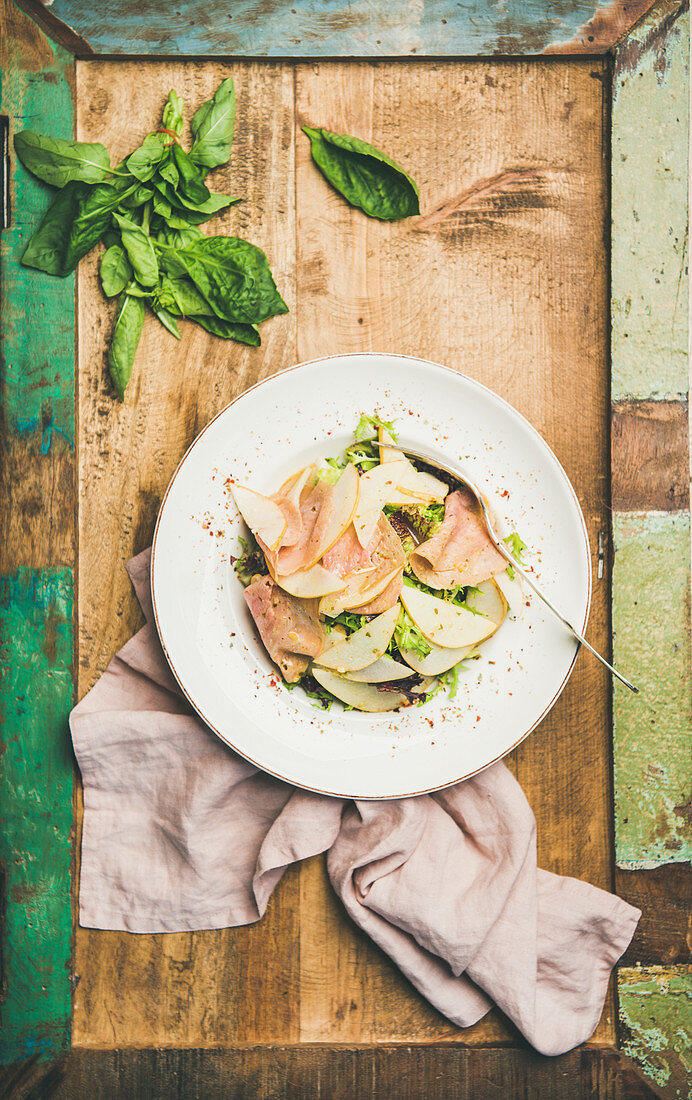Summer salad with smoked turkey ham and pear in white plate over rustic wooden background