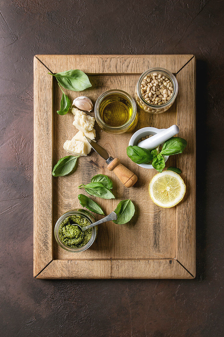 Traditional Basil pesto sauce in glass jar with ingredients above fresh basil, olive oil, parmesan cheese, garlic, pine nuts, lemon