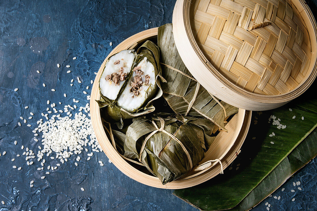 Asian rice piramidal steamed dumplings from rice tapioca flour with meat filling in banana leaves served in bamboo steamer with rice