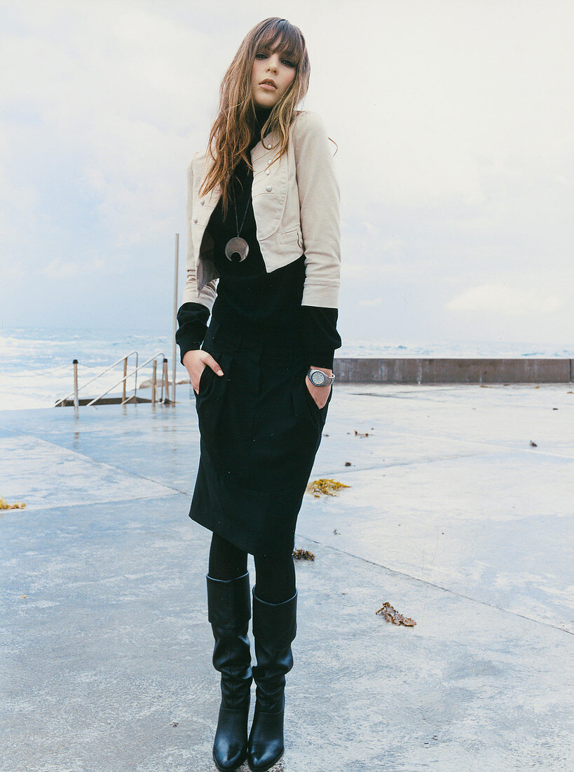 Junge Frau in schwarzem Outfit mit heller Jacke am Meer