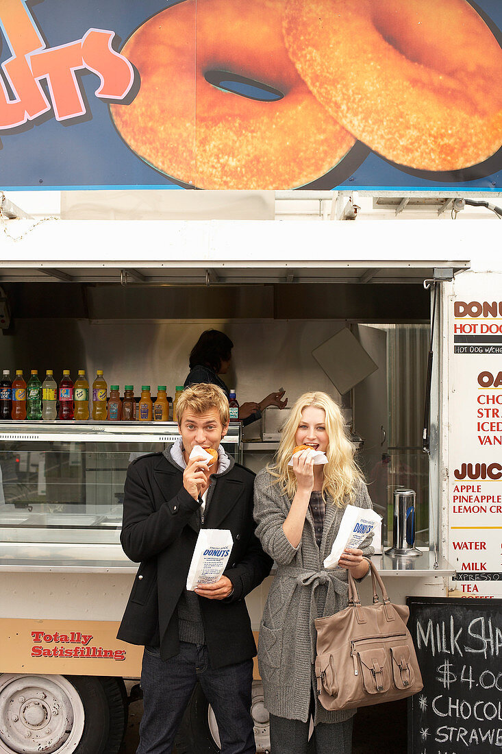 A couple eating doughnuts in front of a food truck