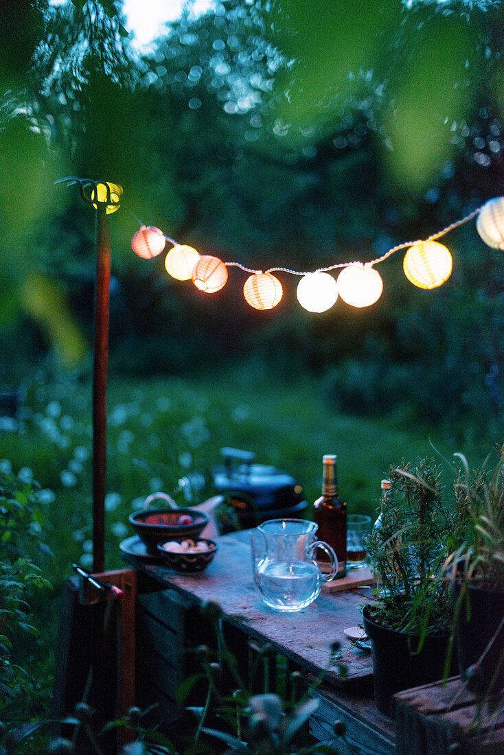 Lampionkette über rustikalem Gartentisch mit Getränken und Snacks