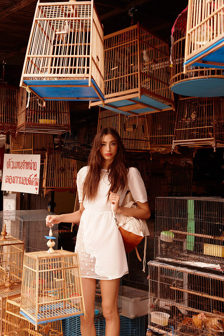 A young woman wearing a white dress holding a bird cage