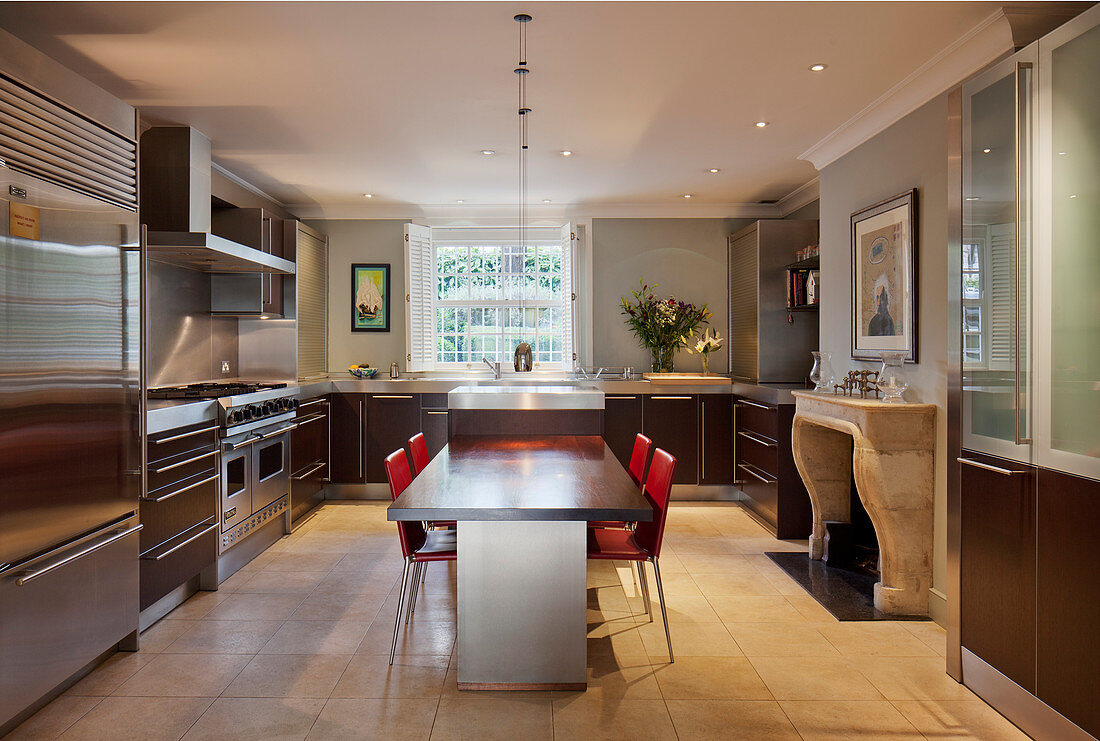 Dining table, red chairs and open fireplace in large modern kitchen