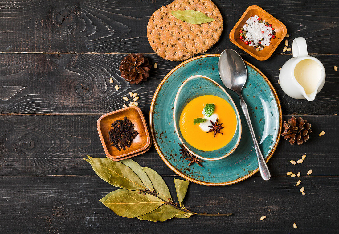 Pumpkin and carrot soup with cream and seasoning in blue bowl on black wooden background, top view