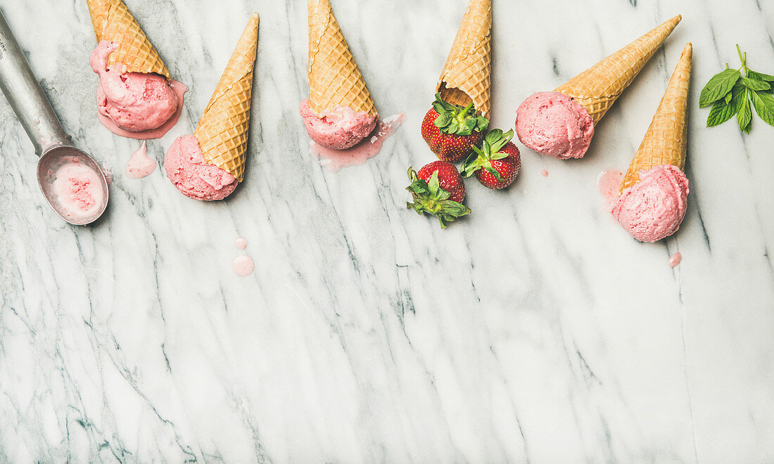 Yogurt ice cream with strawberries in waffle cones over grey marble background