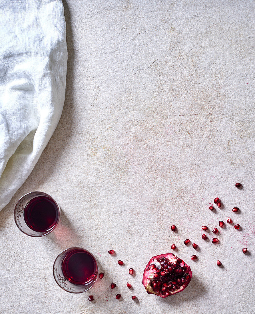 Glasses of red wine and pomegranate wedges with seeds on a white surface