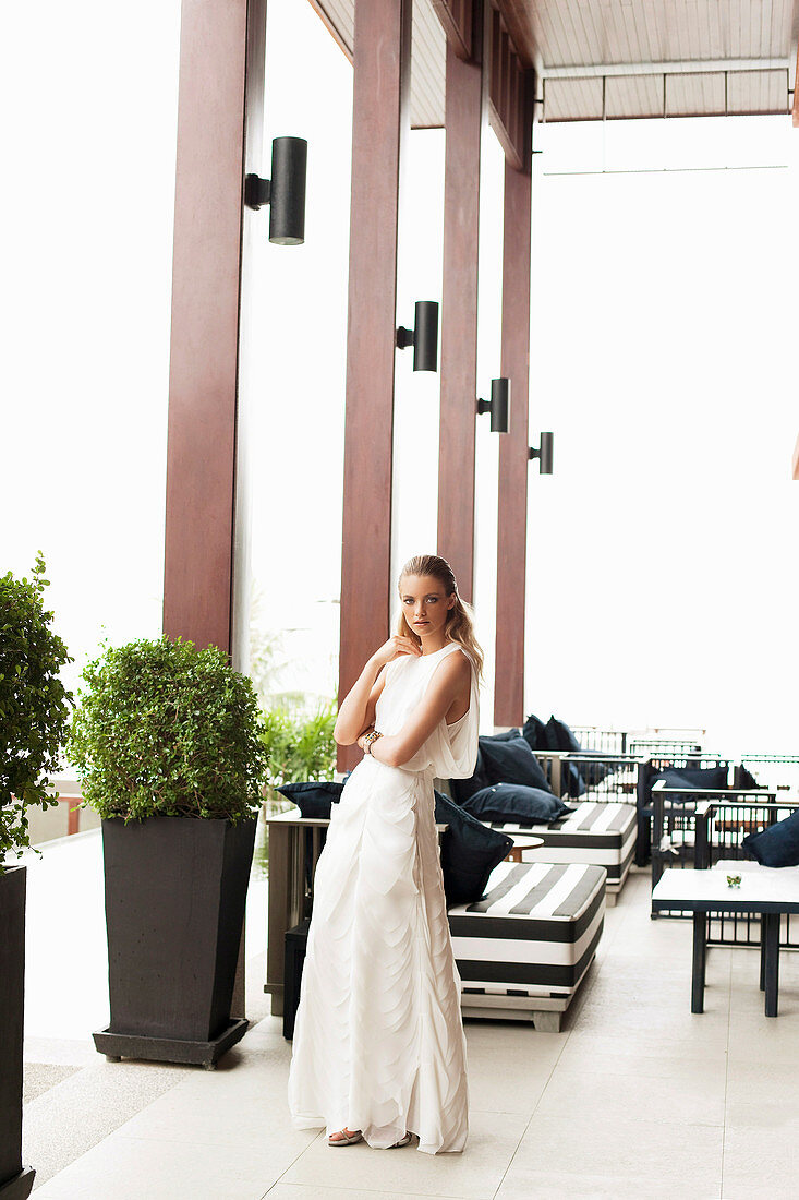 Blonde Frau in elegantem, weißem Kleid auf Terrasse