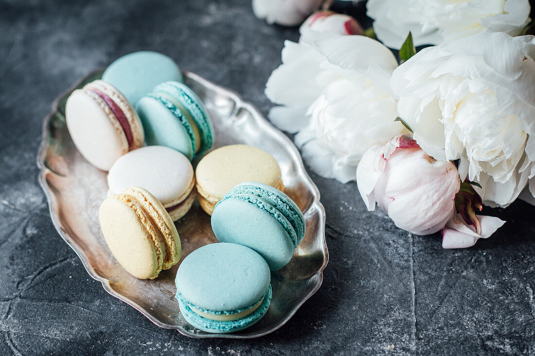 Macarons in Silberschale neben Pfingstrosen