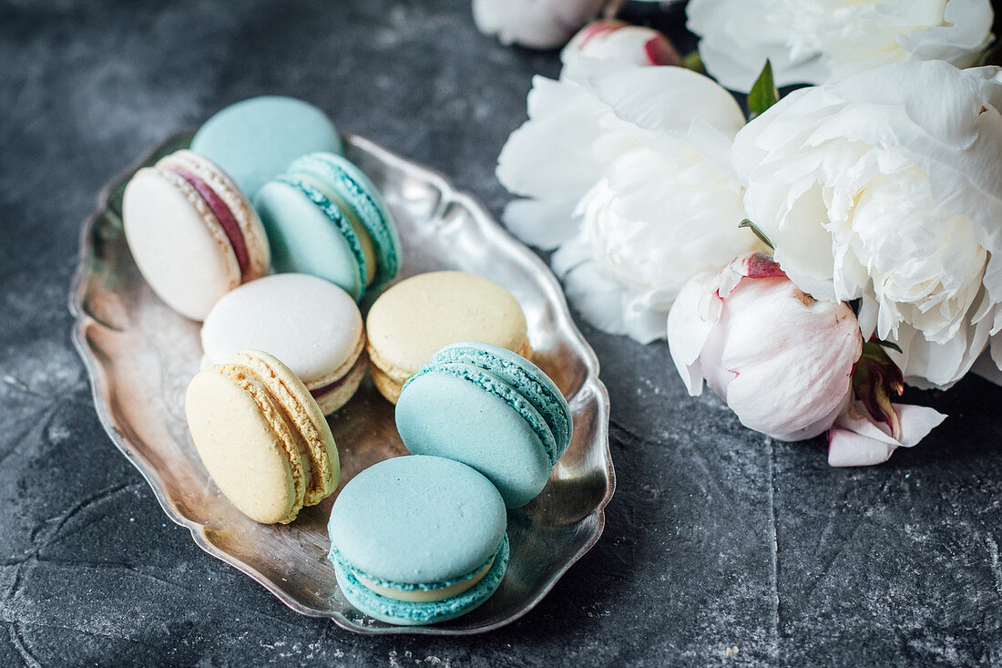Macaroons on a silver dish next to peonies