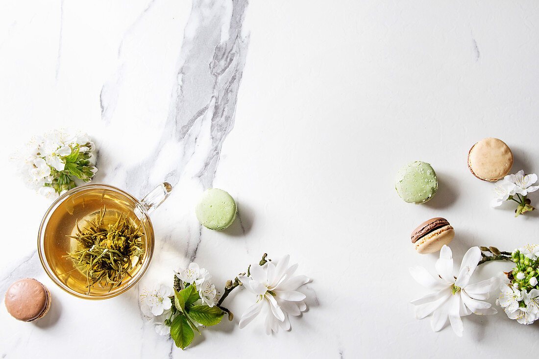 Grüner Tee mit Teeblume in Glastasse, daneben Macarons und Blüten