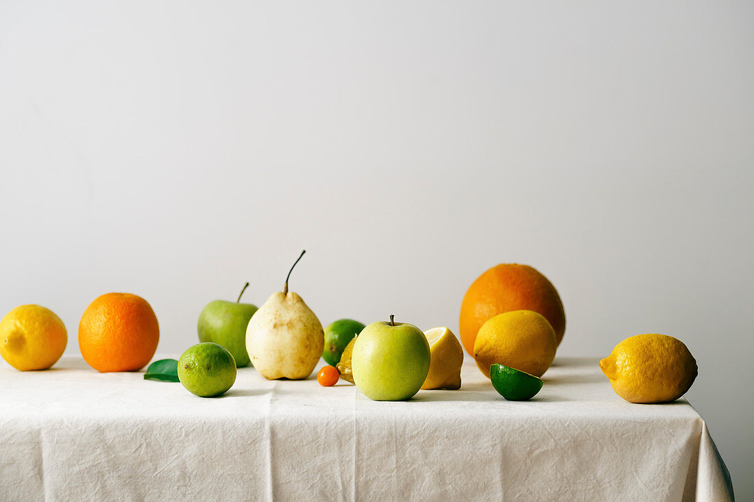 Stillleben mit Zitrusfrüchten, Birnen und Äpfeln auf weisser Tischdecke