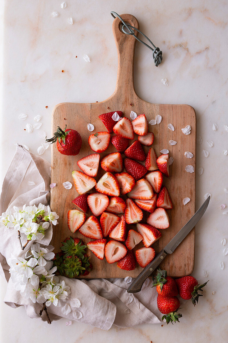 Fresh Strawberries, sliced on a chopping board, surrounded by blossom