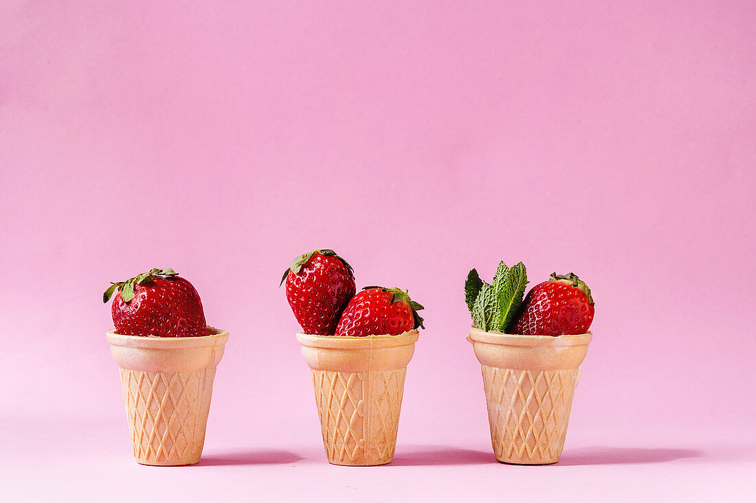 Drei Eistüten gefüllt mit frischen Erdbeeren vor rosa Hintergrund