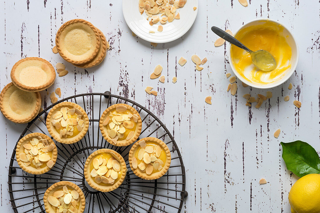 Lemon tartlets decorated with toasted almond flakes, unfilled pastry cases and a bowl of lemon butter