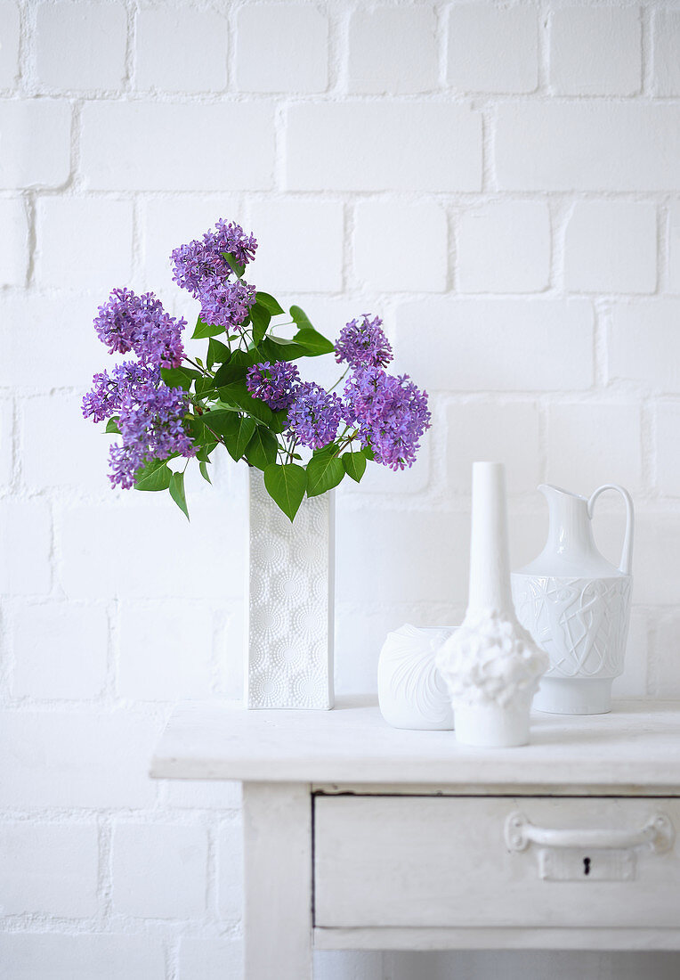 Purple lilac in white vase and other decorative vases