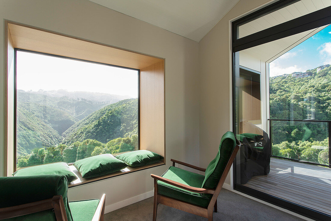 Green armchairs and matching cushions on window seat in panoramic window with view of hilly landscape