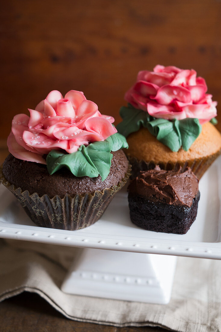 Cupcakes decorated with large sugar roses on a cake stand