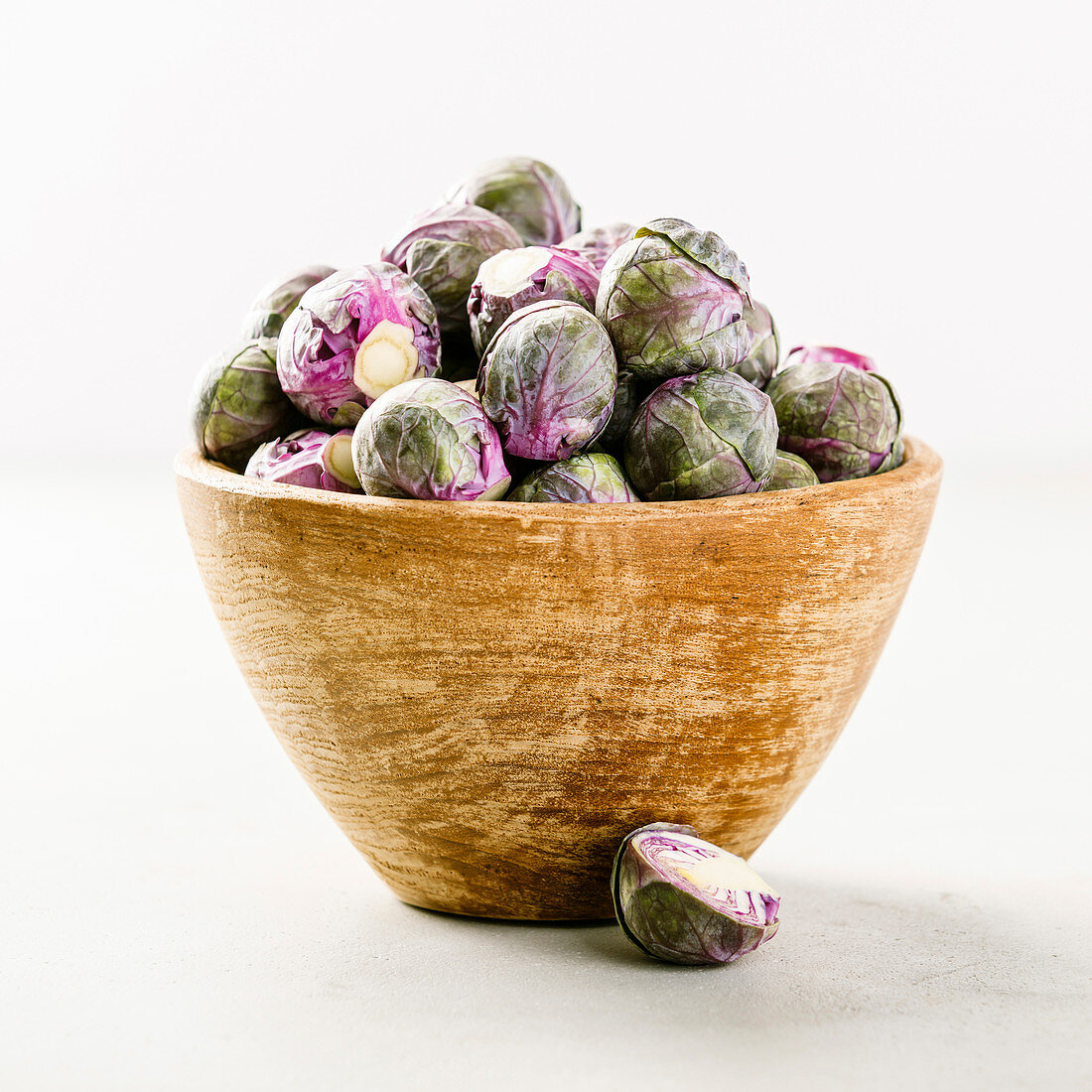 Purple Brussels sprouts in a wooden bowl on concrete background
