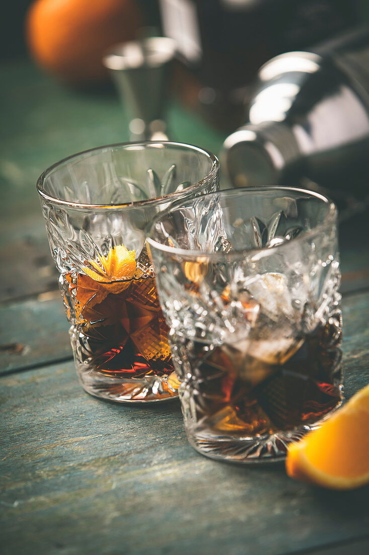 Zwei Cocktail mit Whiskey, Orangenschale und Eis auf Holztisch