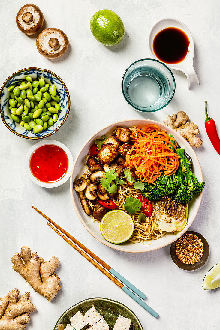 Vegetarian noodles with tofu, broccoli, mushrooms, carrot, bok choy on white stone table