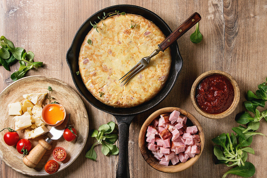 Spanish potato omelette tortilla with bacon served in cast-iron pan with sauce and ingredients