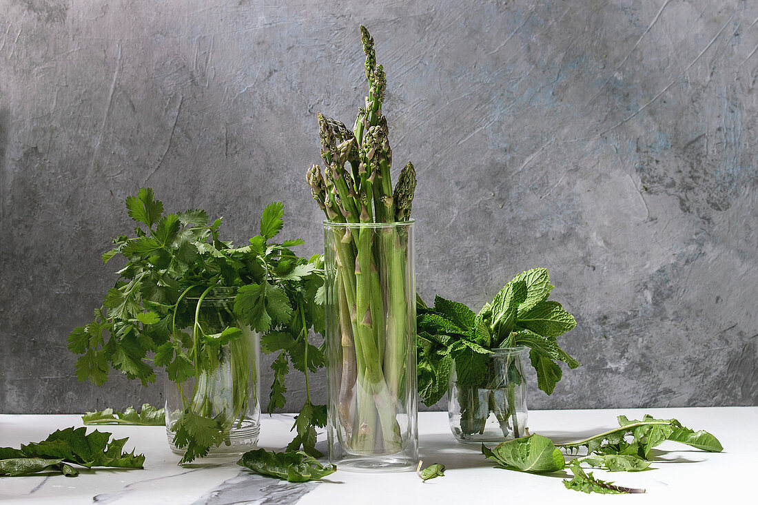Raw uncooked organic green asparagus, bunch of coriander herbs and fresh mint in glass jars