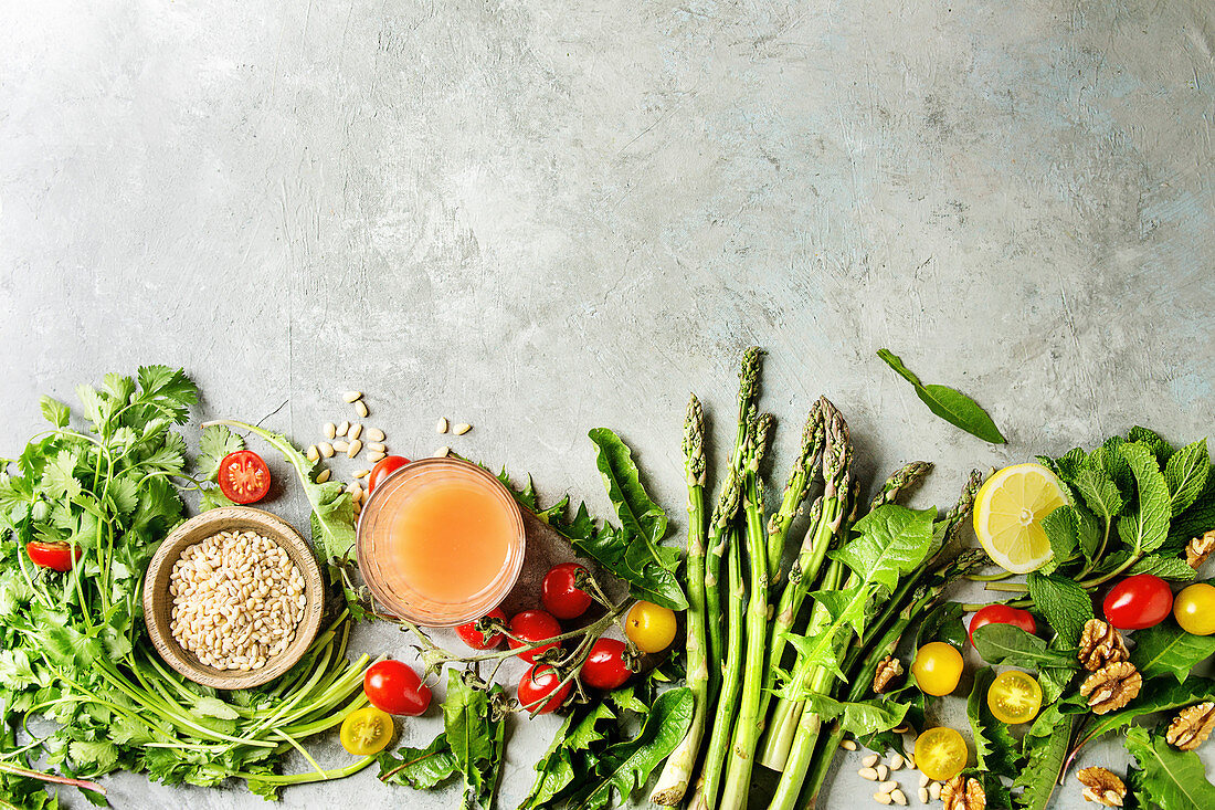 Variety of vegetarian healthy eating food ingredients. Green asparagus, herbs, tomatoes, nuts, wheat corns, dandelion leaves, glass of juice