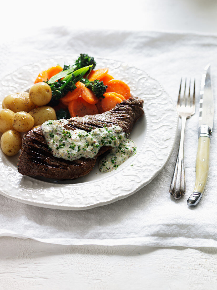A beef steak with potatoes, carrots, broccoli and parsley sauce