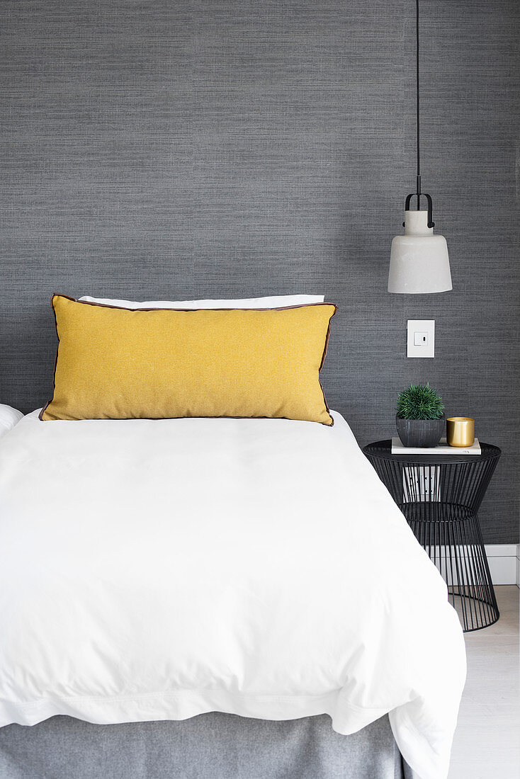 Gelbes Kissen auf dem Bett vor grauer Wand
