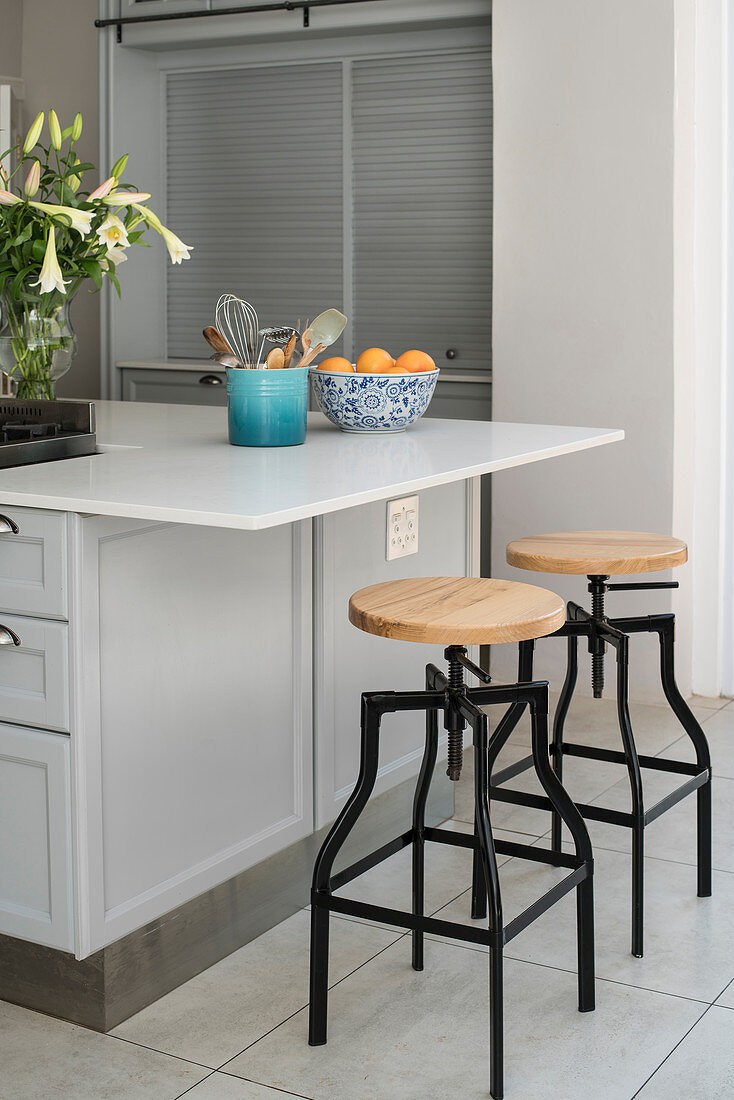 Vase of lilies, kitchen utensils and fruit bowl on island counter with barstools